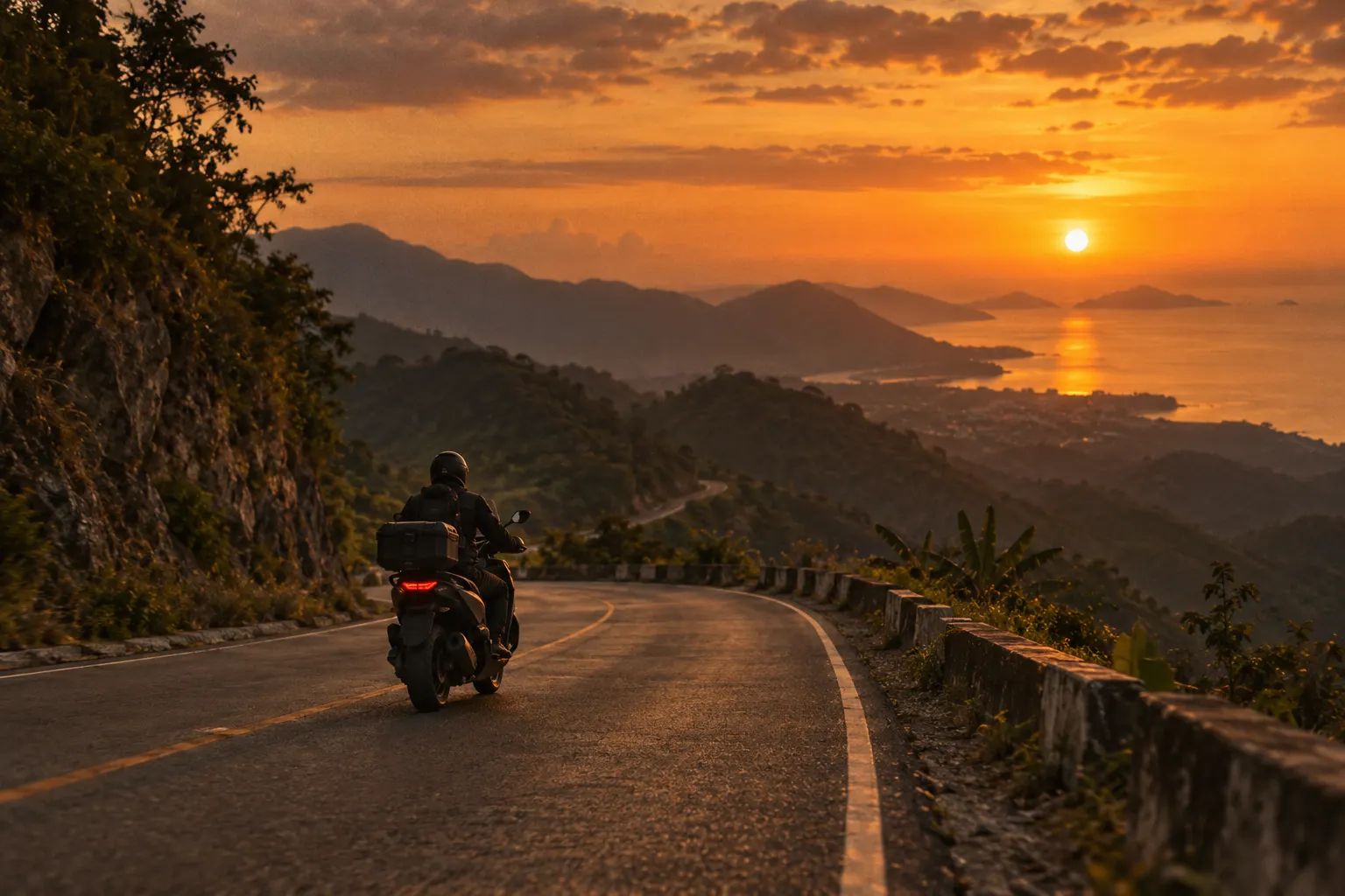 Rider on a winding mountain road above the sea at sunset